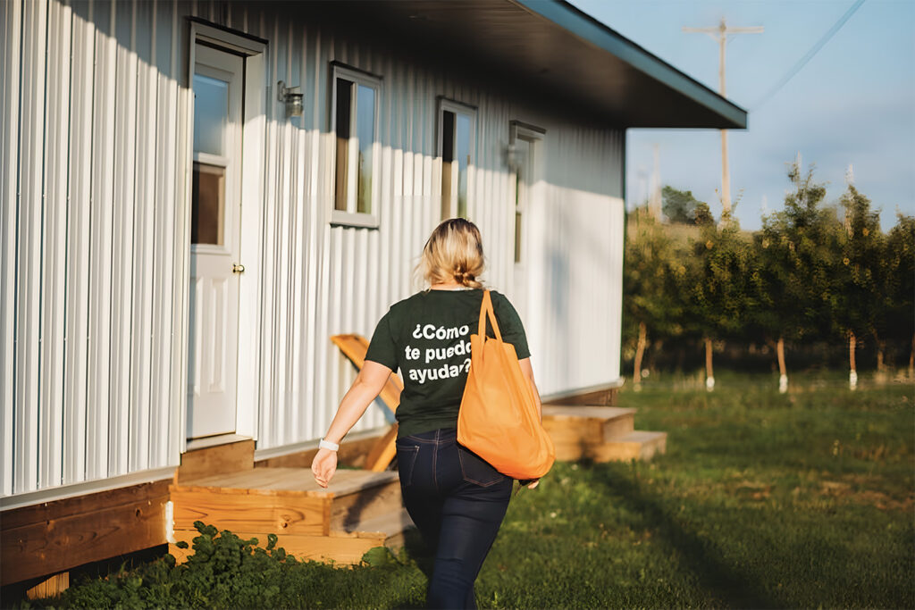 white woman walking in trailer park with shirt that says como te puedo ayudar